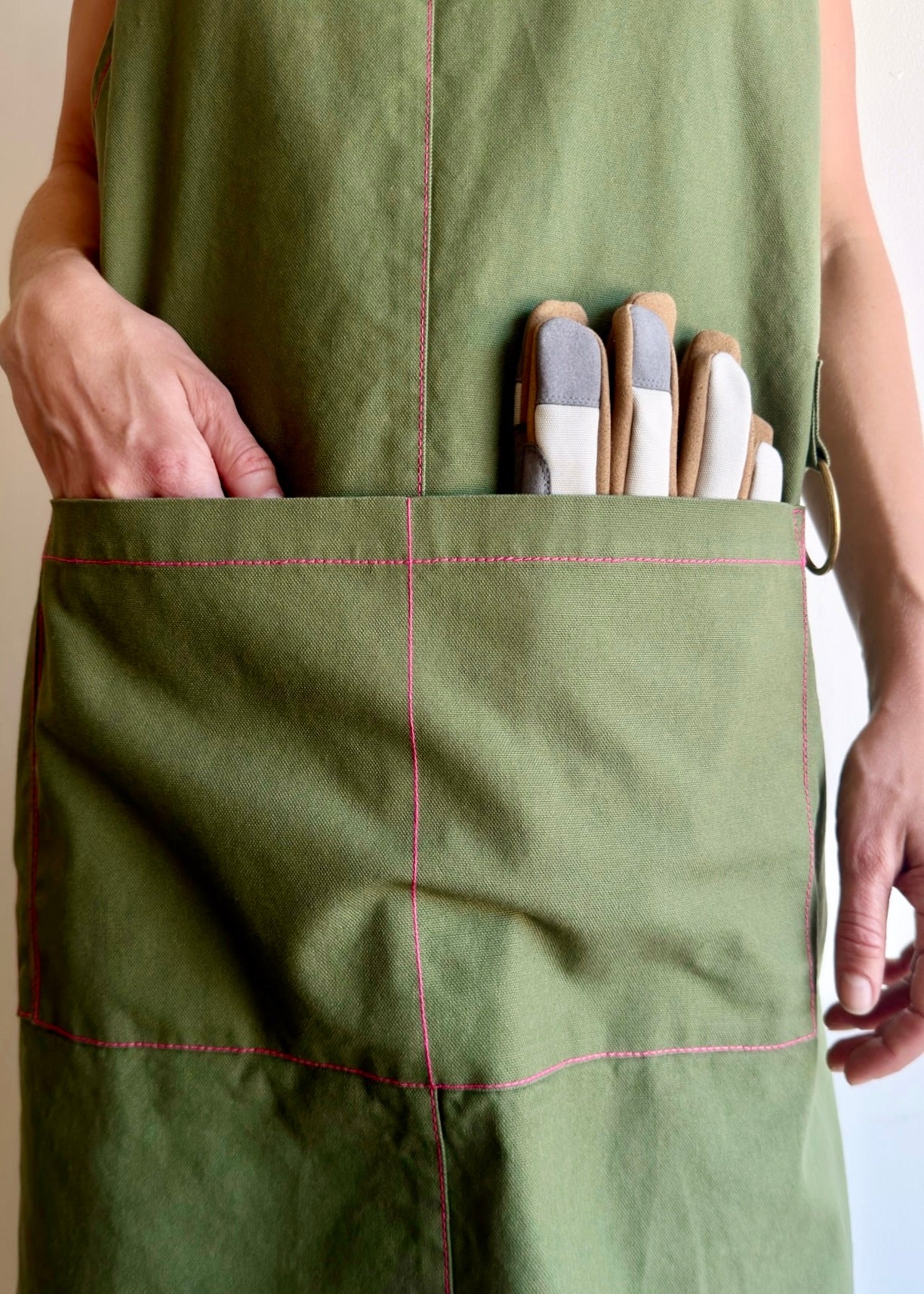 Model wearing Flora Animalia organic canvas harvest apron in grass green, pocket detail.