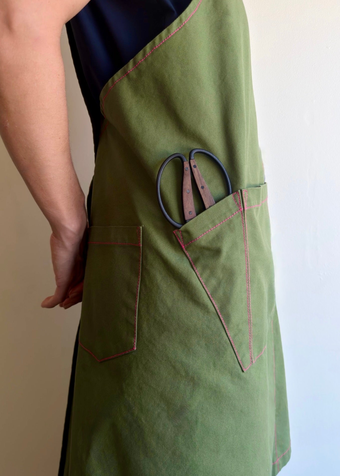 Model wearing Flora Animalia organic canvas harvest apron in grass green, side tool pocket detail.