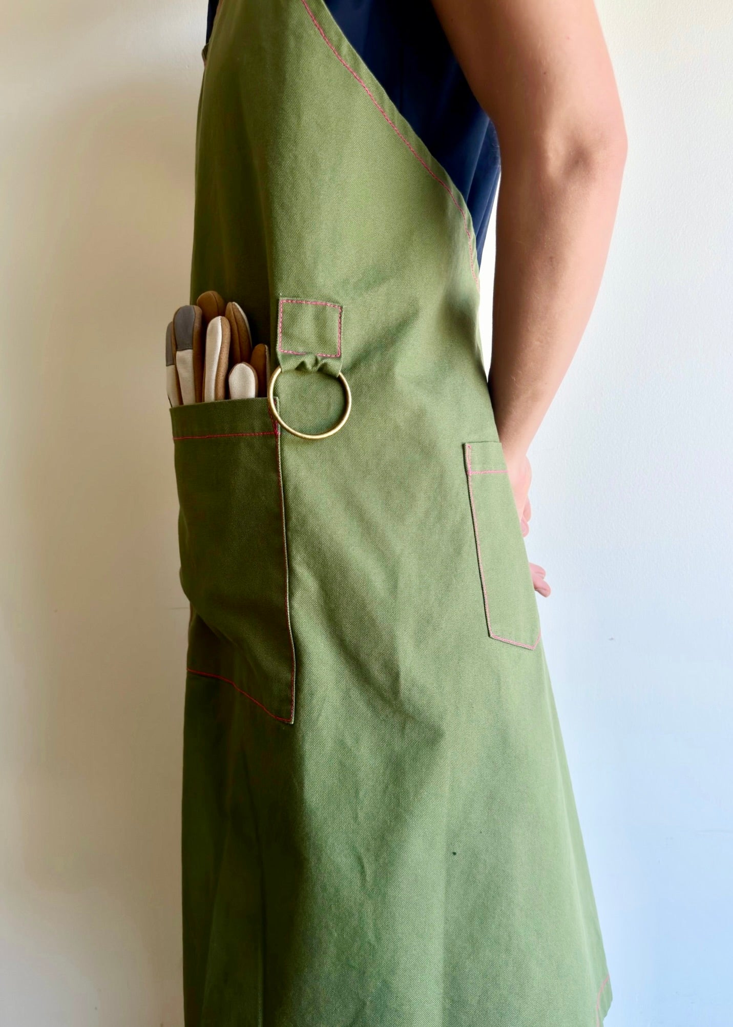 Model wearing Flora Animalia organic canvas harvest apron in grass green, pocket and hardware detail.