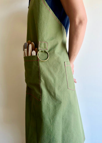 Model wearing Flora Animalia organic canvas harvest apron in grass green, pocket and hardware detail.