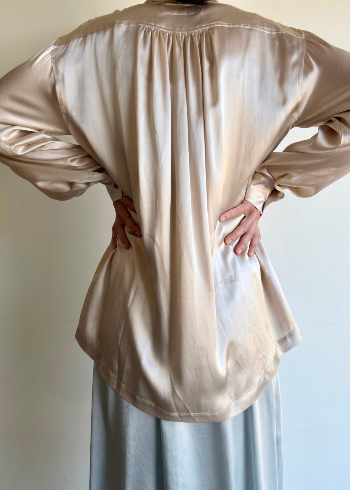 rear view of satiny biosilk agnes shirt with pleated yolk and model's hands on waist