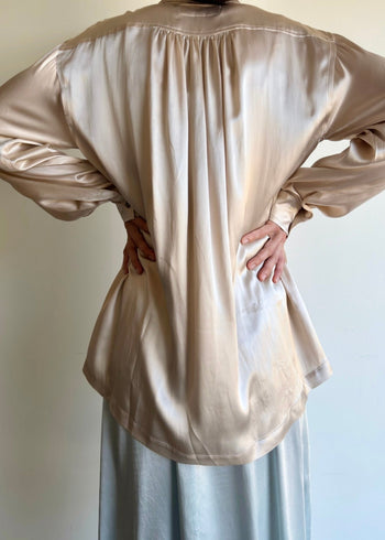 rear view of satiny biosilk agnes shirt with pleated yolk and model's hands on waist