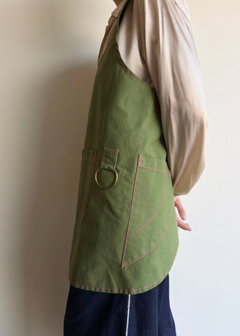 Person wearing a green apron, showing tool pockets and utility ring .