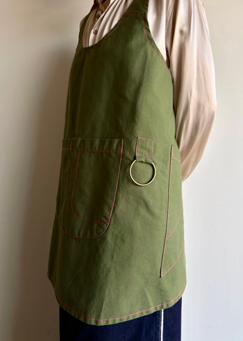 Person wearing a grass green apronette, showing tool pockets and utility ring .