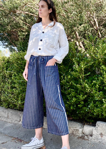 blue and white striped denim cropped drawstring pants with white button down top. Hand in pocket