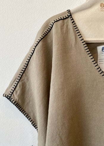 close up Beige v-neck shirt with black trim on a white background