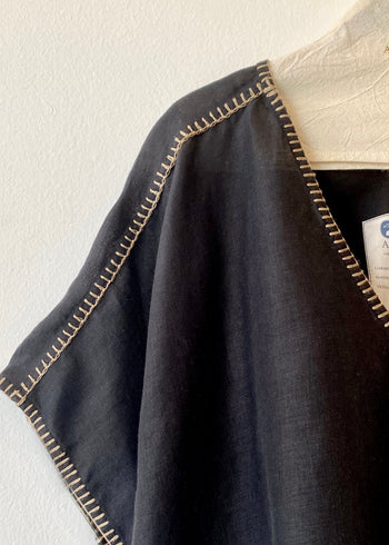 black linen garment with tan stitching on a white background