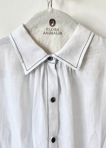 closeup detail White shirt collar with black stitching on a hanger with 'Flora Animalia' branding.