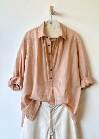Pink shirt with rolled-up sleeves on a hanger against a white wall