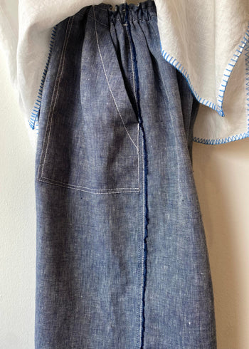 side tight image of Blue linen pants worn over a beige shirt on a neutral background