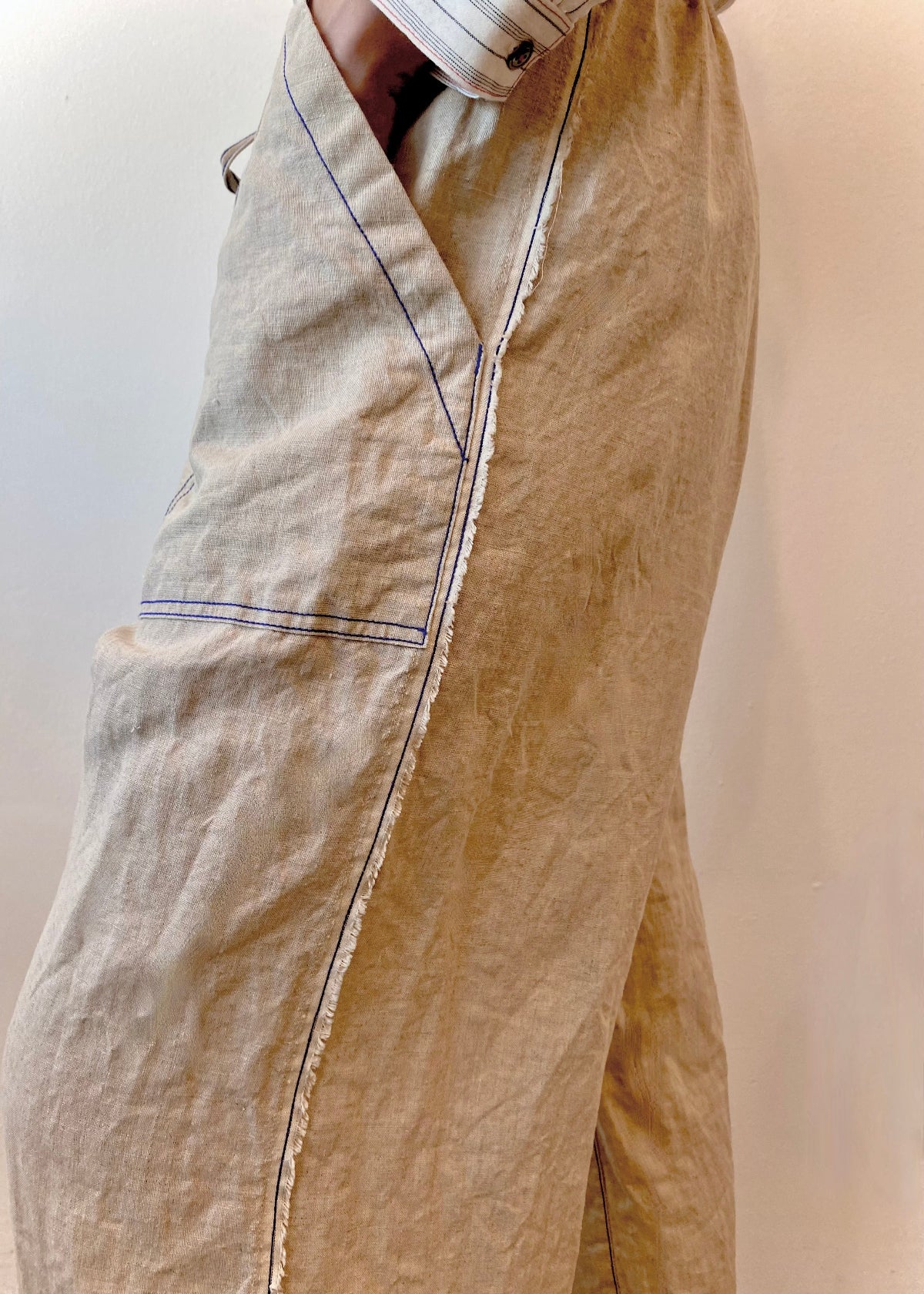Beige pants with black stitching and raw edge on a plain background