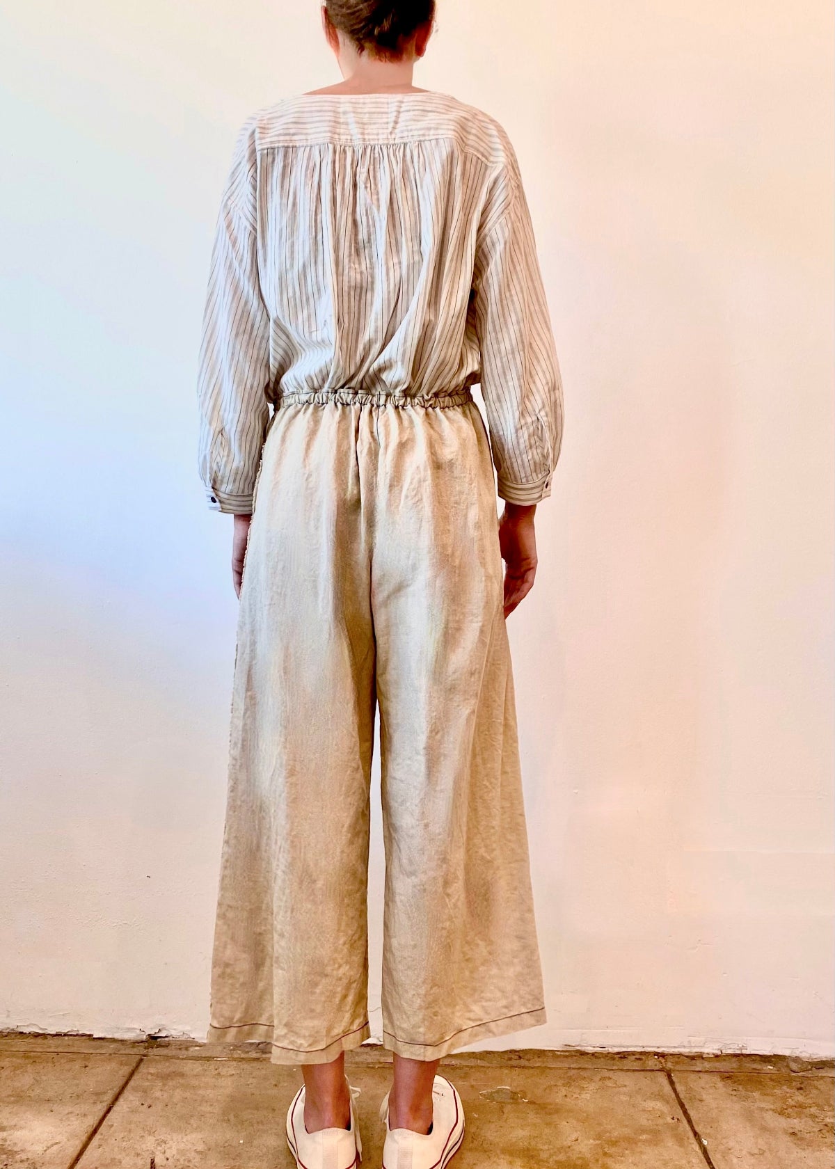 Person wearing a striped long-sleeve top and beige wide-leg pants against a white wall.