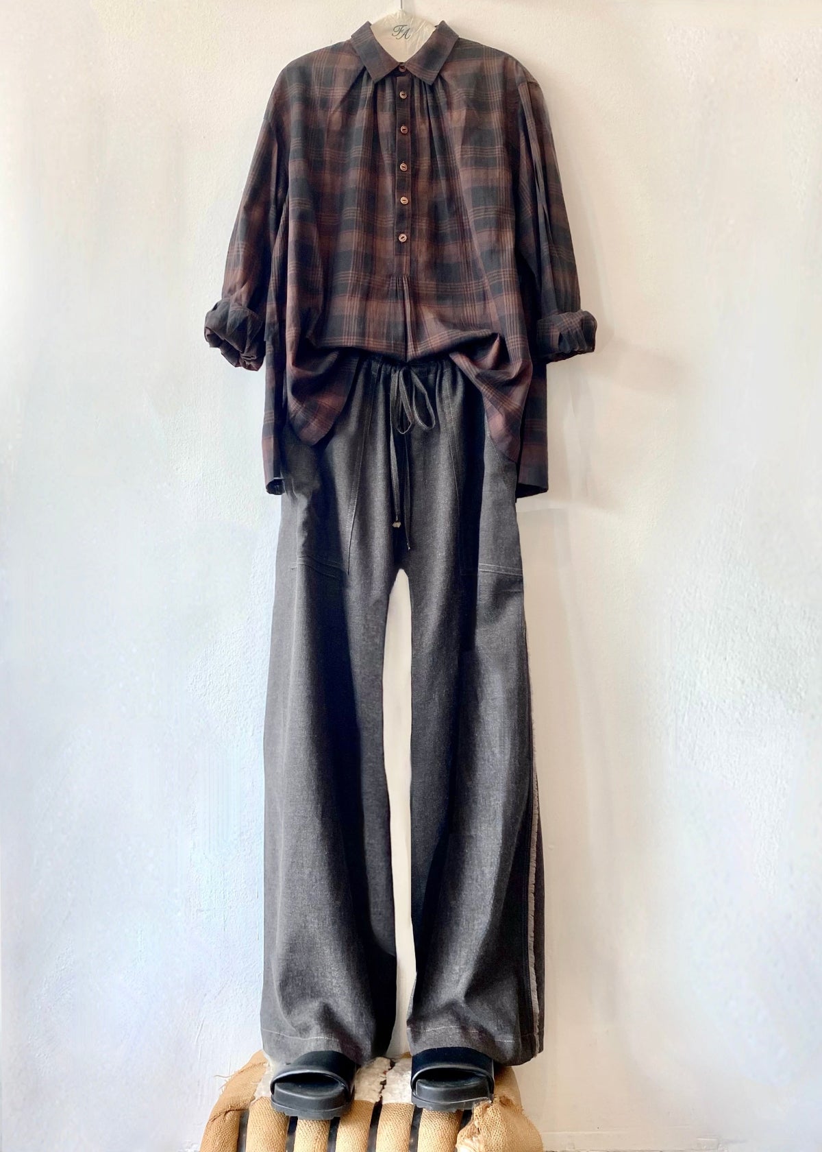 extra long dark drawstring pants and plaid top hanging against a white wall
