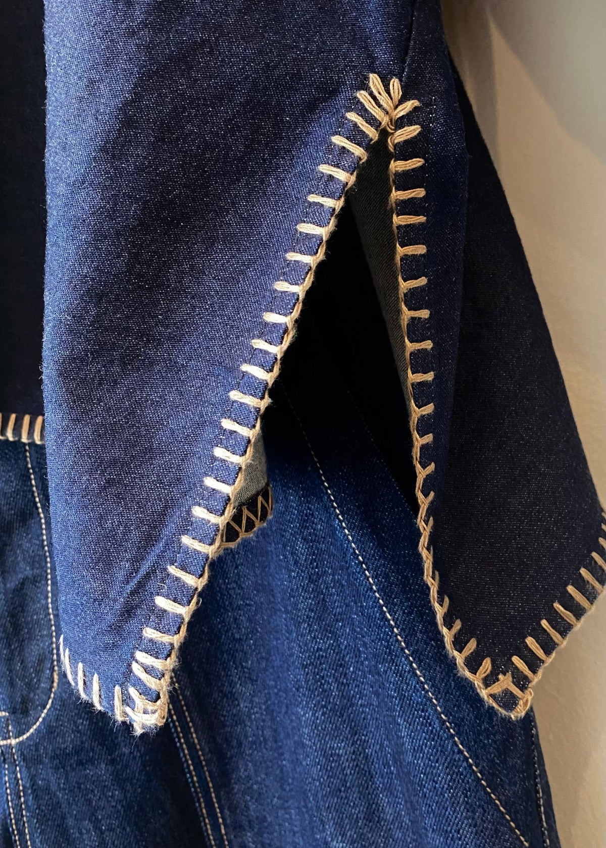 Close-up of blue denim fabric with tan blanket stitching on a plain background