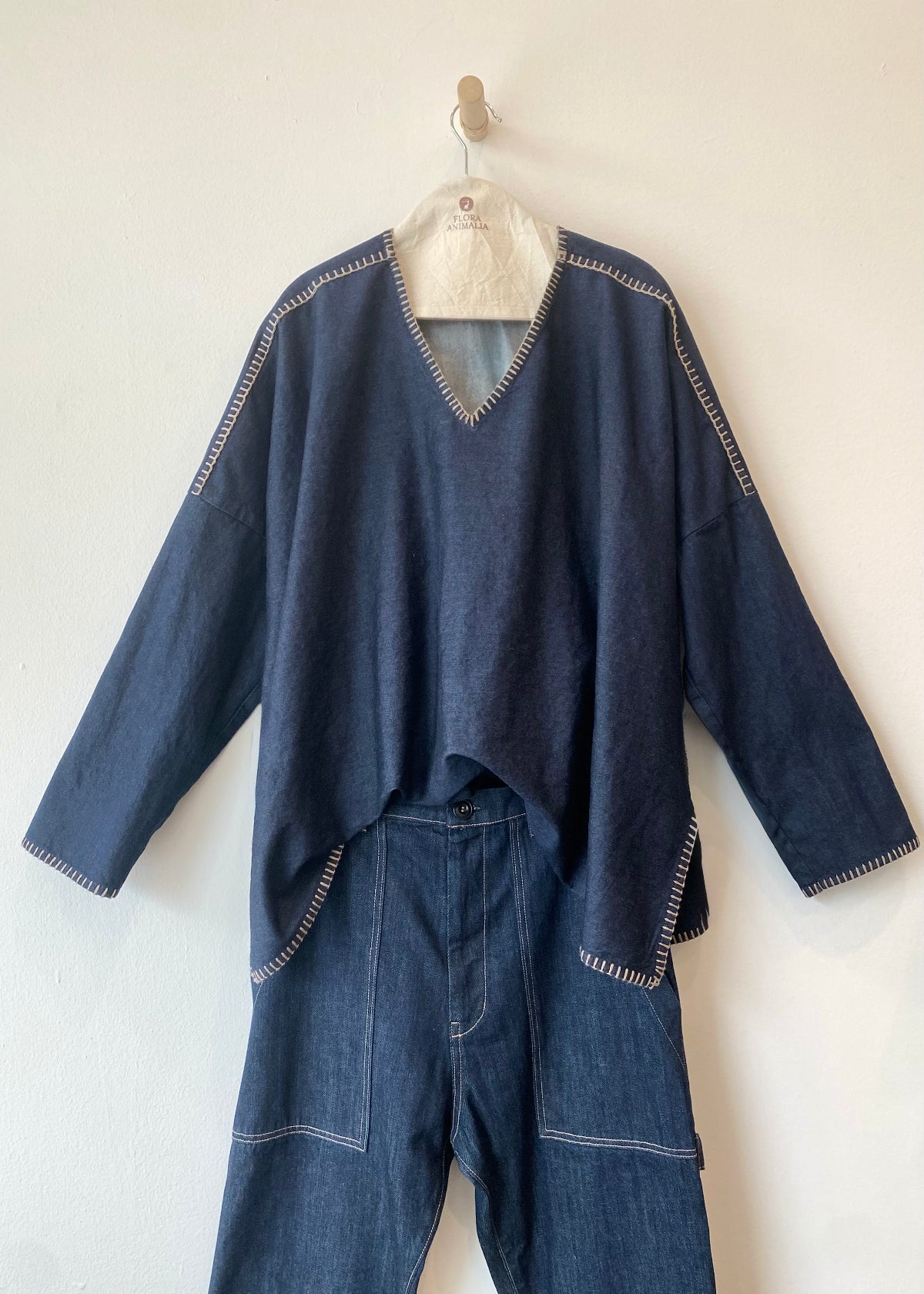 Blue denim outfit with a top and pants on a hanger against a white wall.