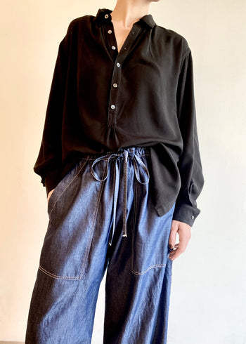 Person wearing a black button Agnes shirt and drawstring blue denim jeans against a plain background