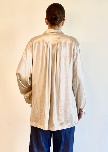 Rear view of person wearing a beige long-sleeve shirt with pleated yoke against a plain background
