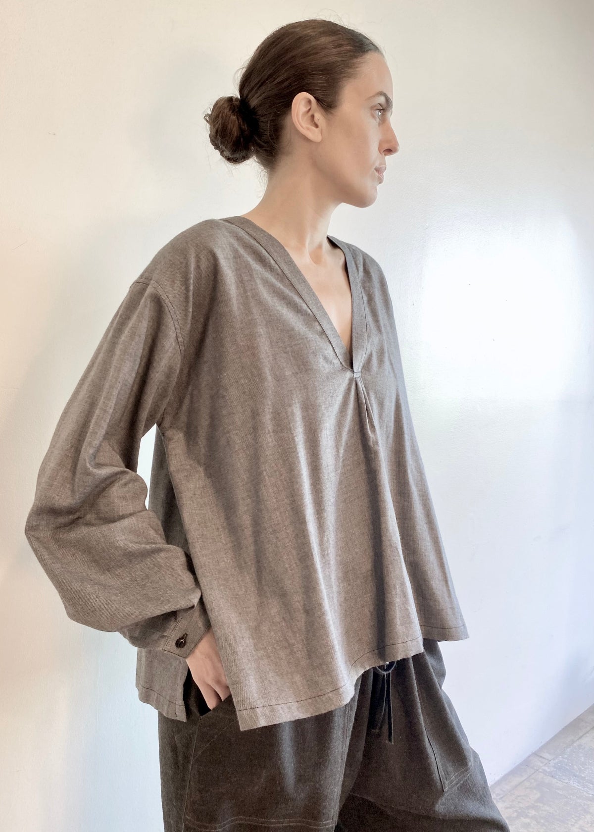 Woman wearing a light gray Farmer's Smock with dark gray drawstring flannel pants against a plain background