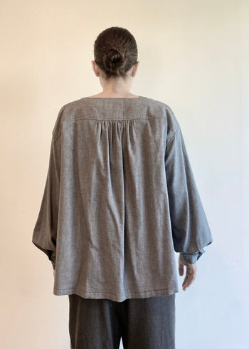 Rear view of a model wearing a light gray Farmer's Smock with pleated yolk and pants against a plain background