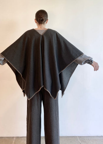 rear view of Person wearing a dark gray poncho over a matching gray pants outfit against a plain background
