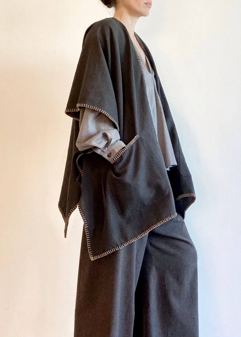 Woman wearing a light gray Farmer's Smock with dark gray drawstring flannel pants against a plain background