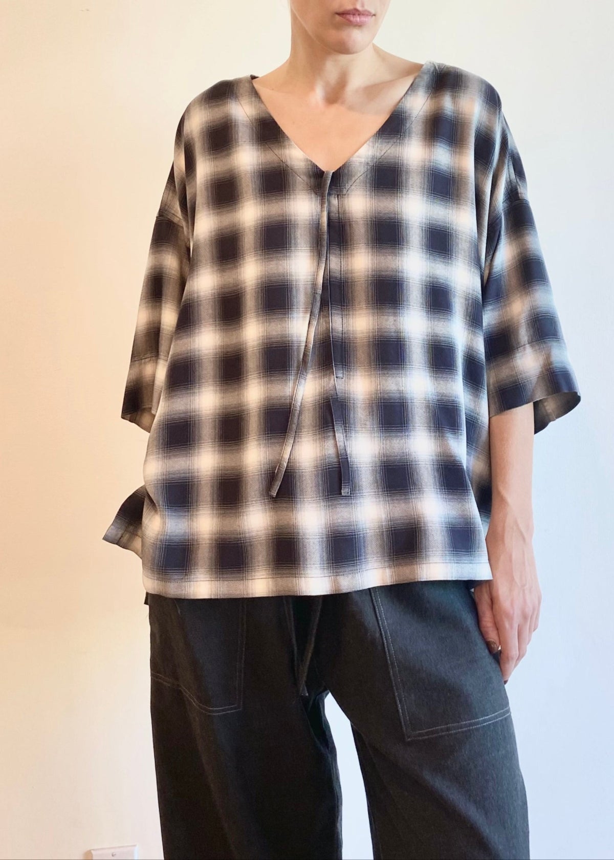 Woman wearing a plaid v-neck shirt and dark pants against a plain background