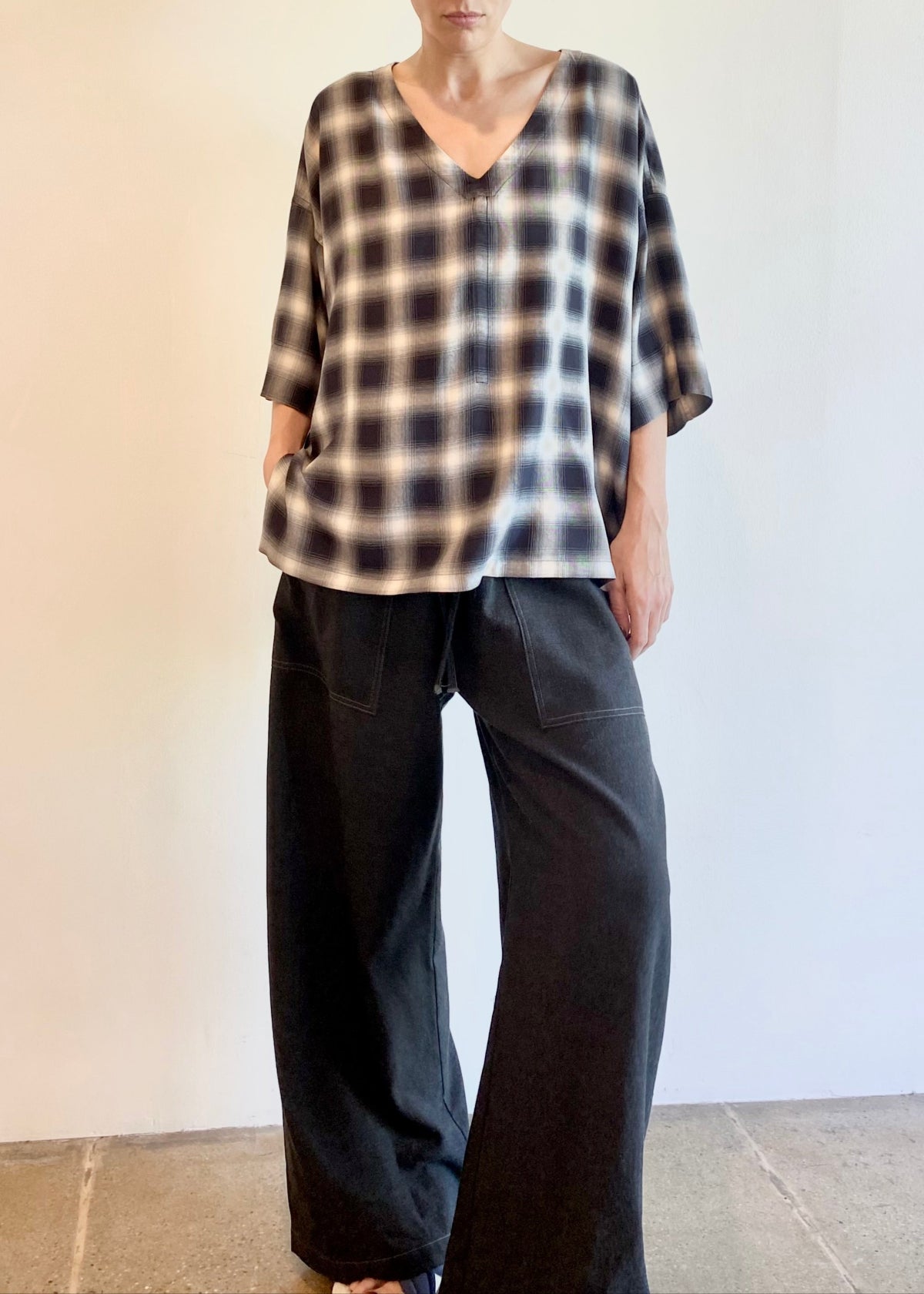 Woman wearing a plaid v-neck shirt and dark pants against a plain background