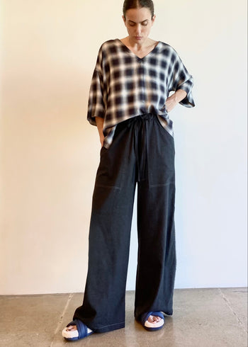 Person wearing a plaid v-neck shirt and grey wide-leg pants against a plain background