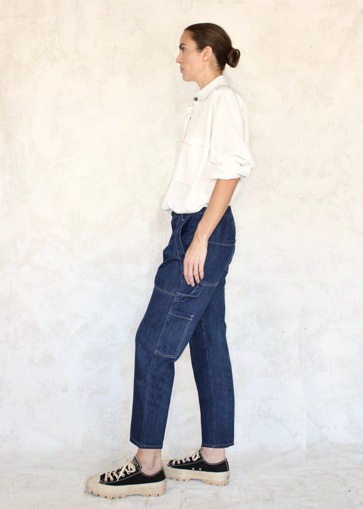 Side view of Model wearing white button down shirt and cropped indigo denim Maker's pant