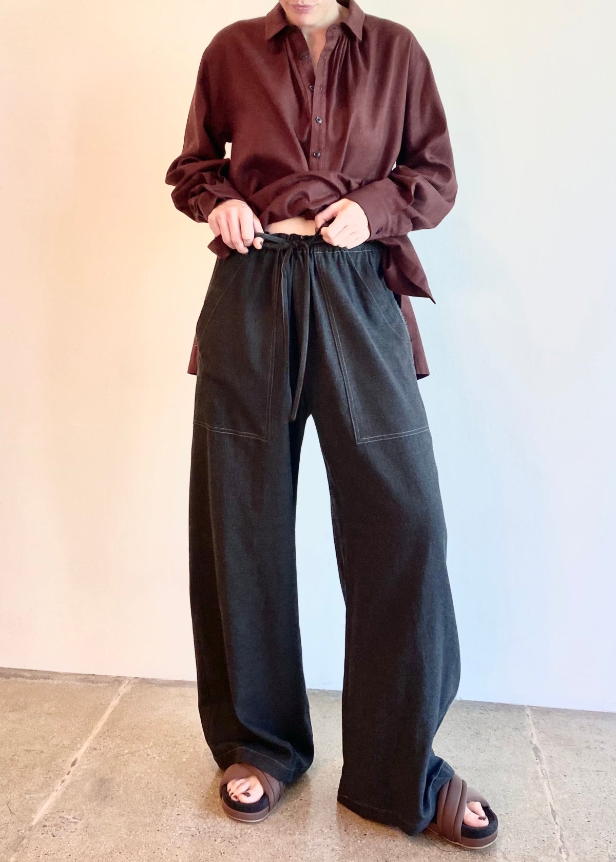 Person wearing a brown shirt and dark pants against a plain background