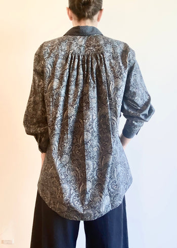 rear view of Person wearing a paisley patterned Agnes shirt and dark gray pants on a neutral background