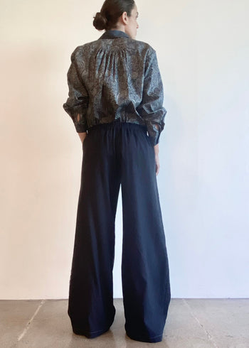 rear of Person wearing a patterned shirt and navy pants wide against a plain background