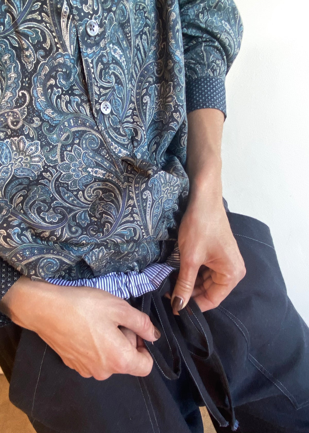 striped waist band detail of pants  Person wearing a paisley patterned shirt and dark pants with a white background