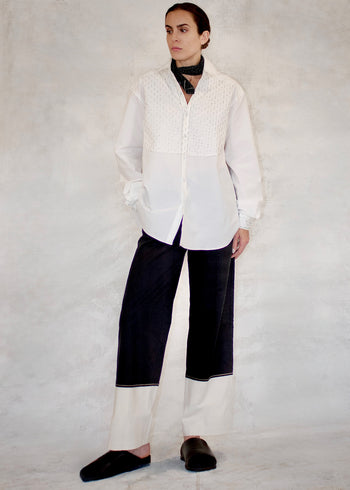 Person wearing a white shirt and black pants with white on lower letgs on a plain background