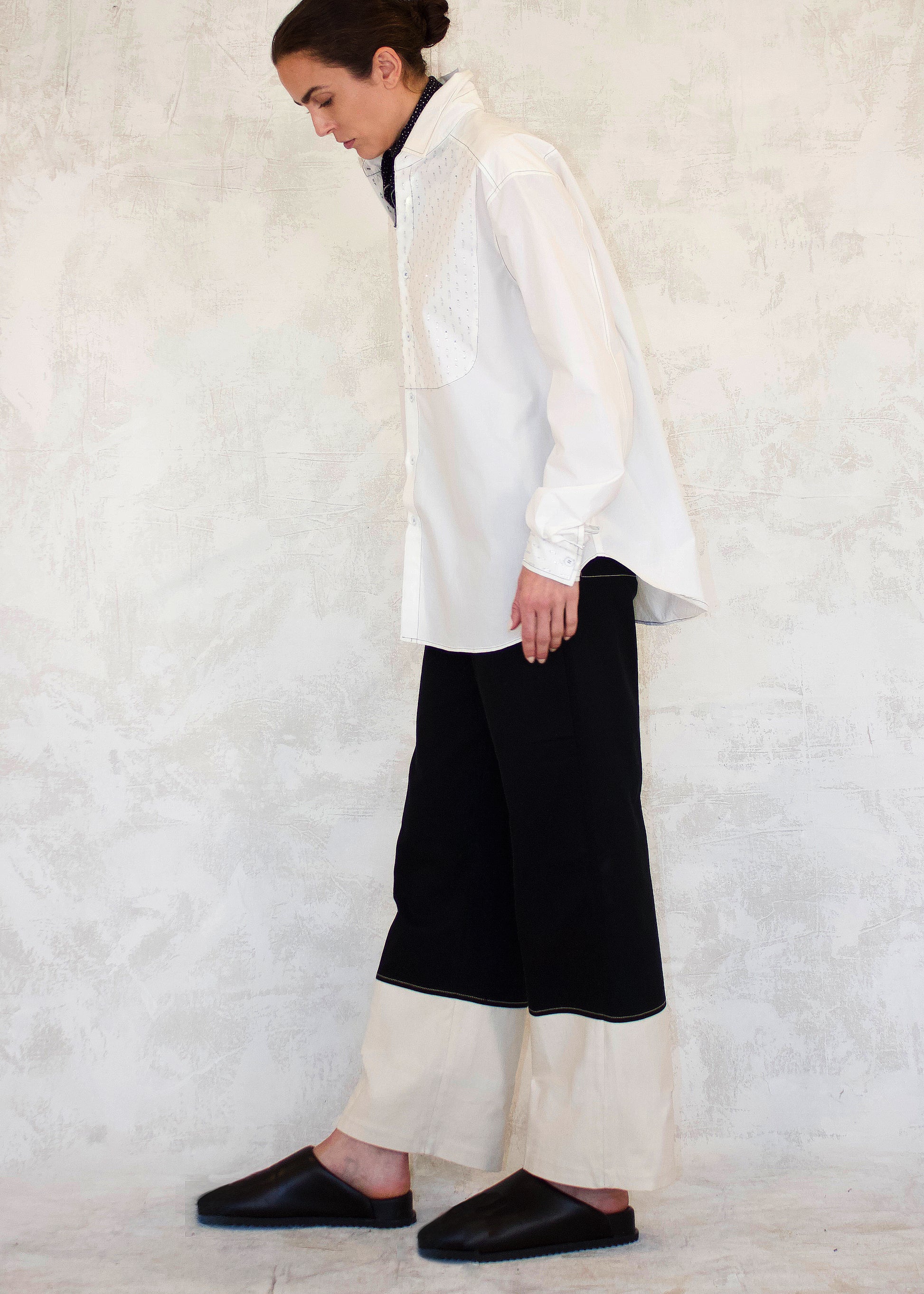 Person wearing a white shirt and black pants against a textured white wall