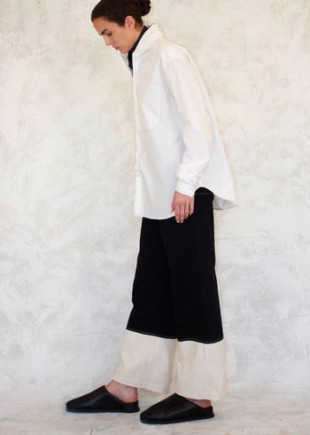 Person wearing a white shirt and black pants against a textured white wall