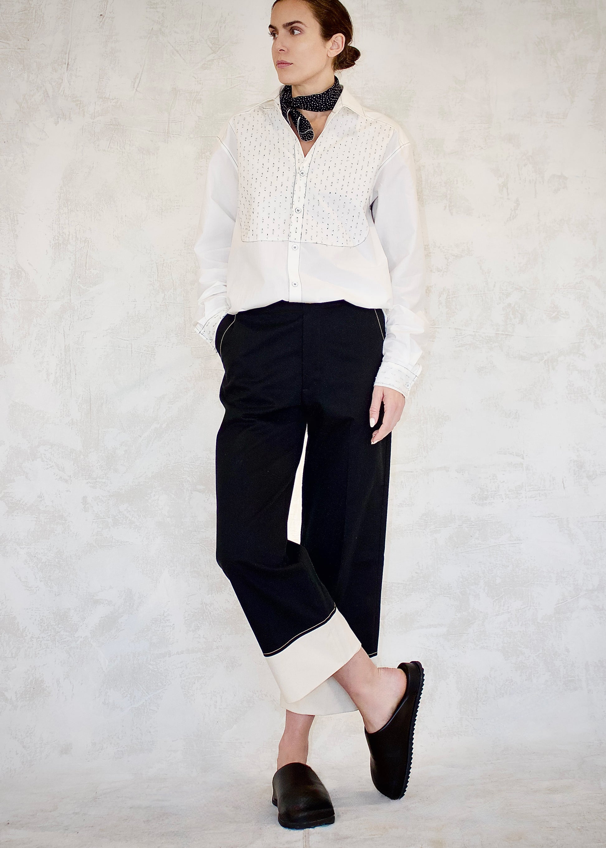 Person wearing a white button top with silver metal dot detailing, black block pants with white cuffs, and black shoes on a light gray background