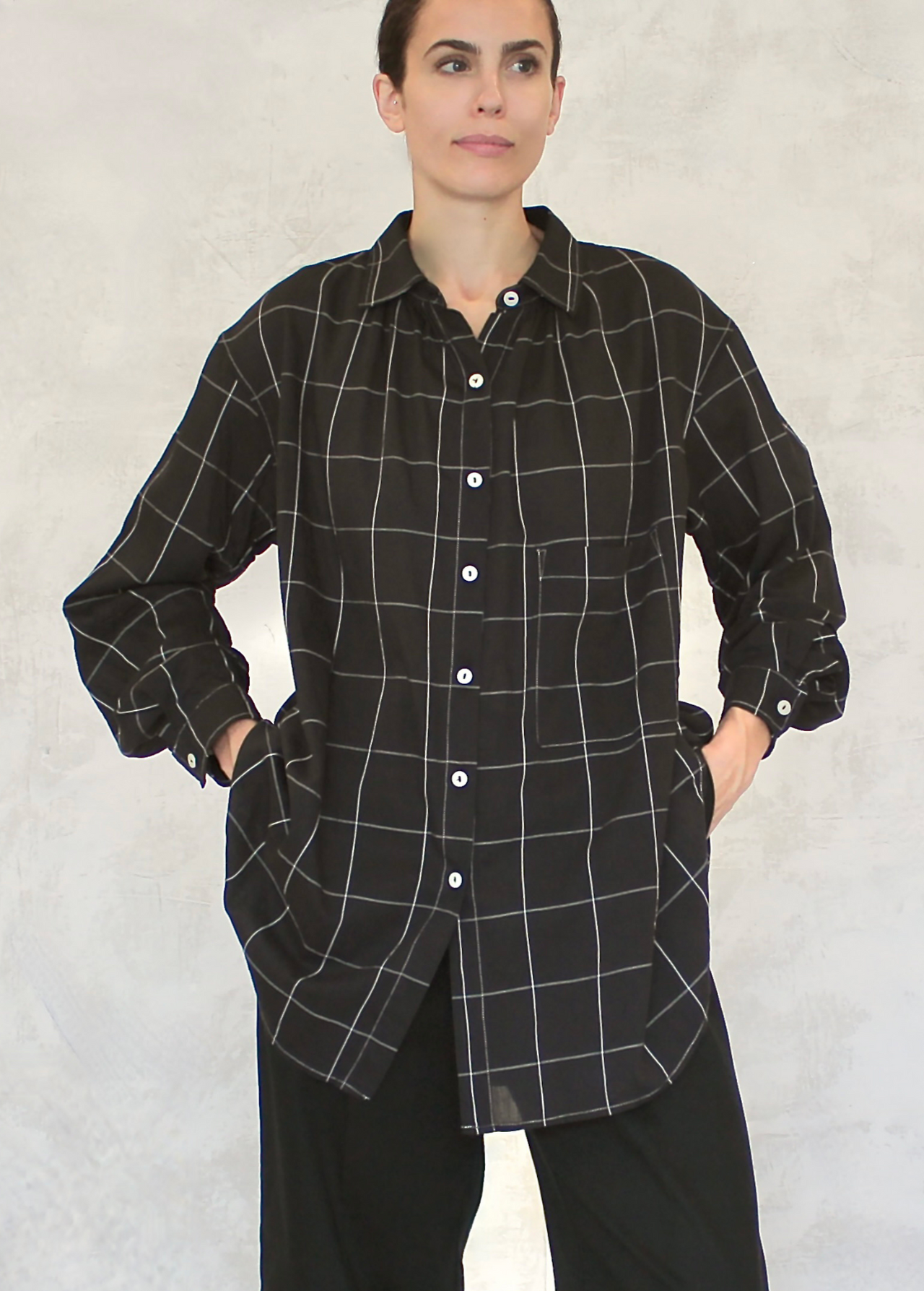 A person wearing a classic black and white checkered artist shirt with a collar, two front pockets, and button front placket.