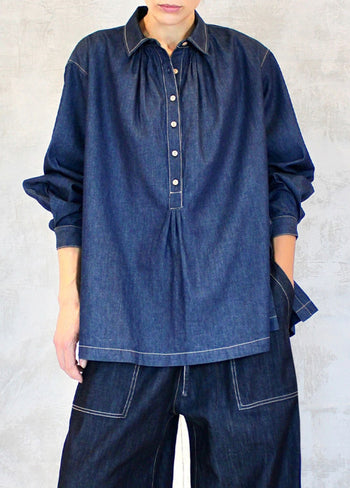 A person wearing a long-sleeved, button-up denim shirt with a classic collar, in a blue color, against a white background.