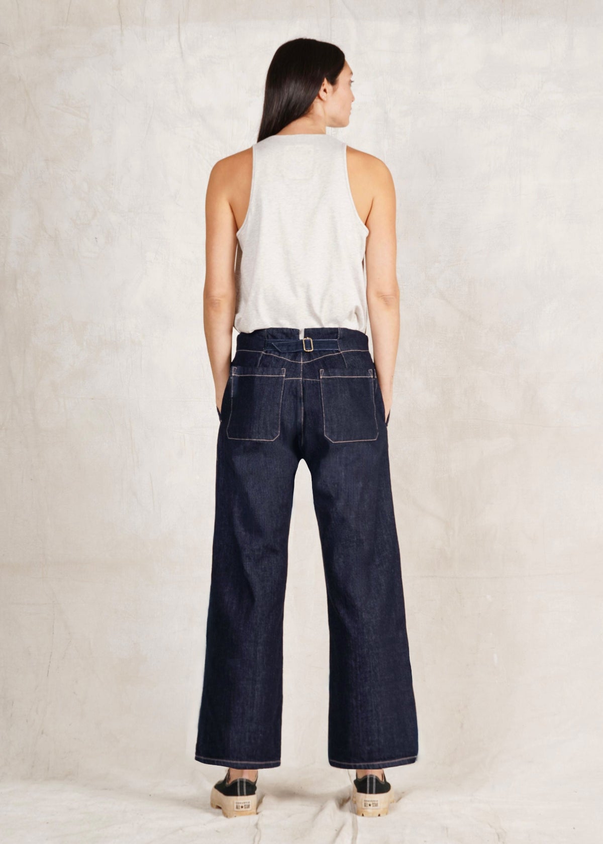 rear view of a Person wearing a white sleeveless top and Artist Pant indigo jeans on a plain background