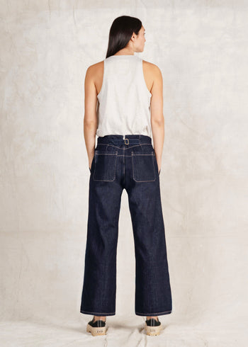 rear view of a Person wearing a white sleeveless top and Artist Pant indigo jeans on a plain background