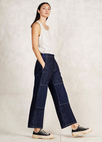 Woman wearing dark blue jeans and a white top against a plain background
