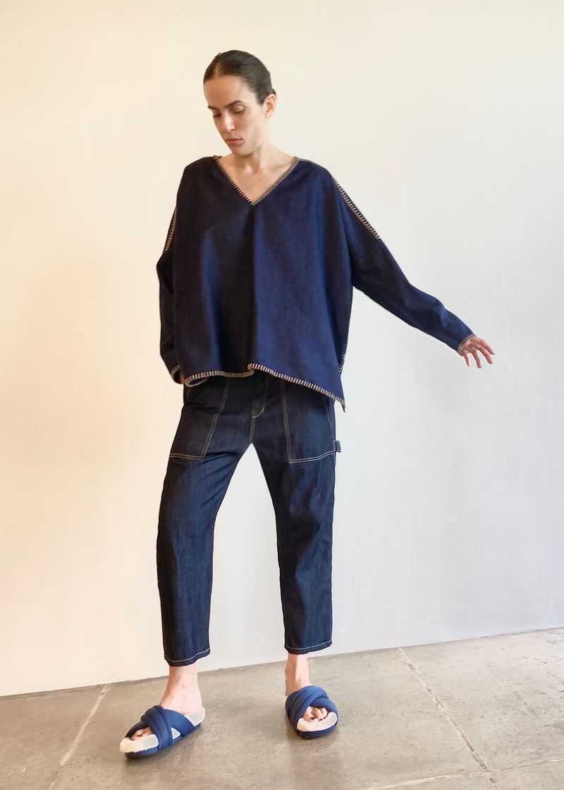 Person wearing a navy blue denim poncho sh and jeans standing against a plain background