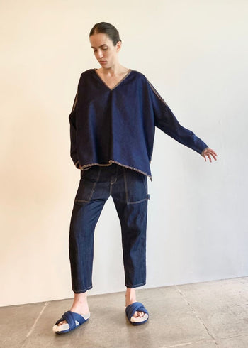 Person wearing a navy blue denim poncho sh and jeans standing against a plain background